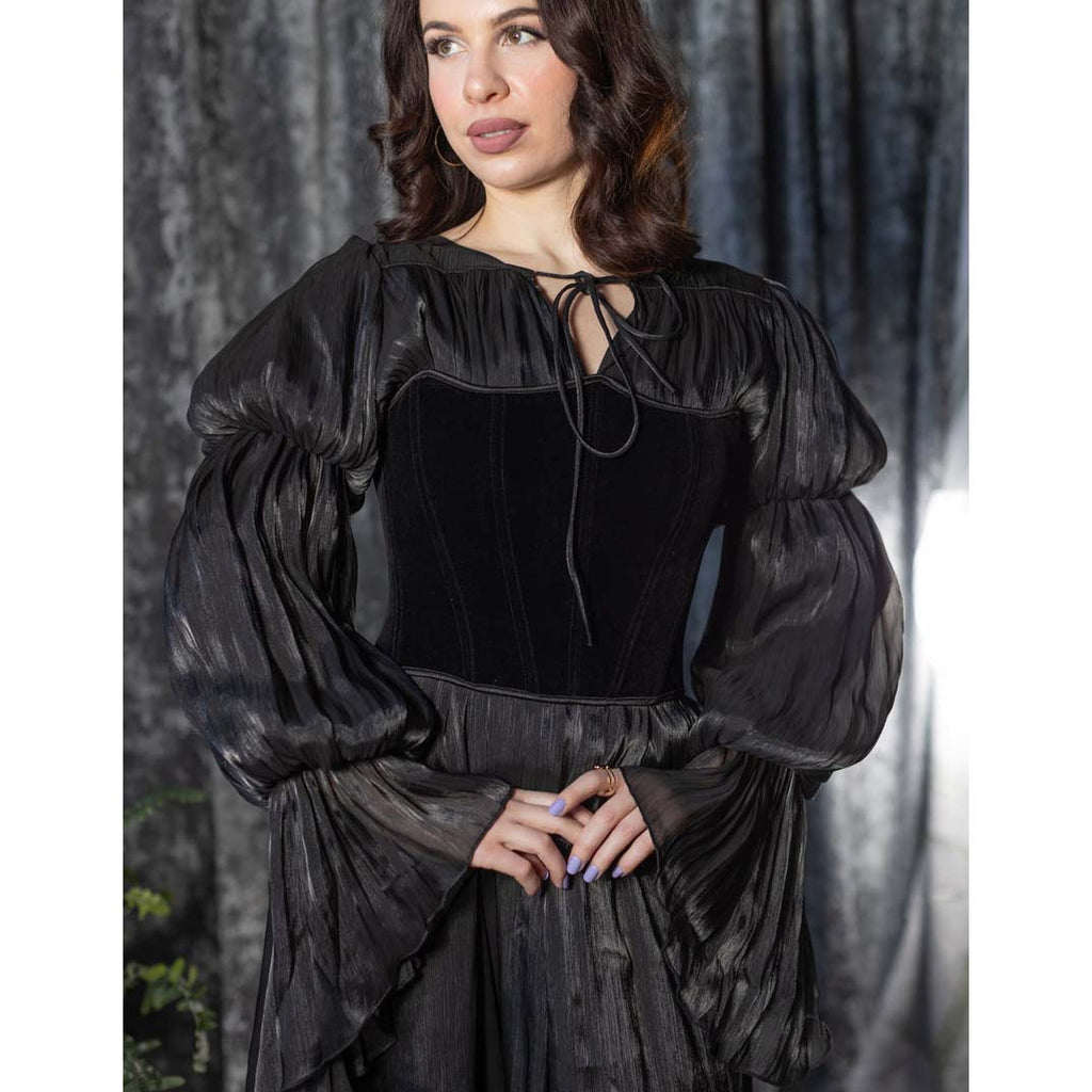 Woman wearing a black velvet dress with puffed sleeves against a dark curtain background