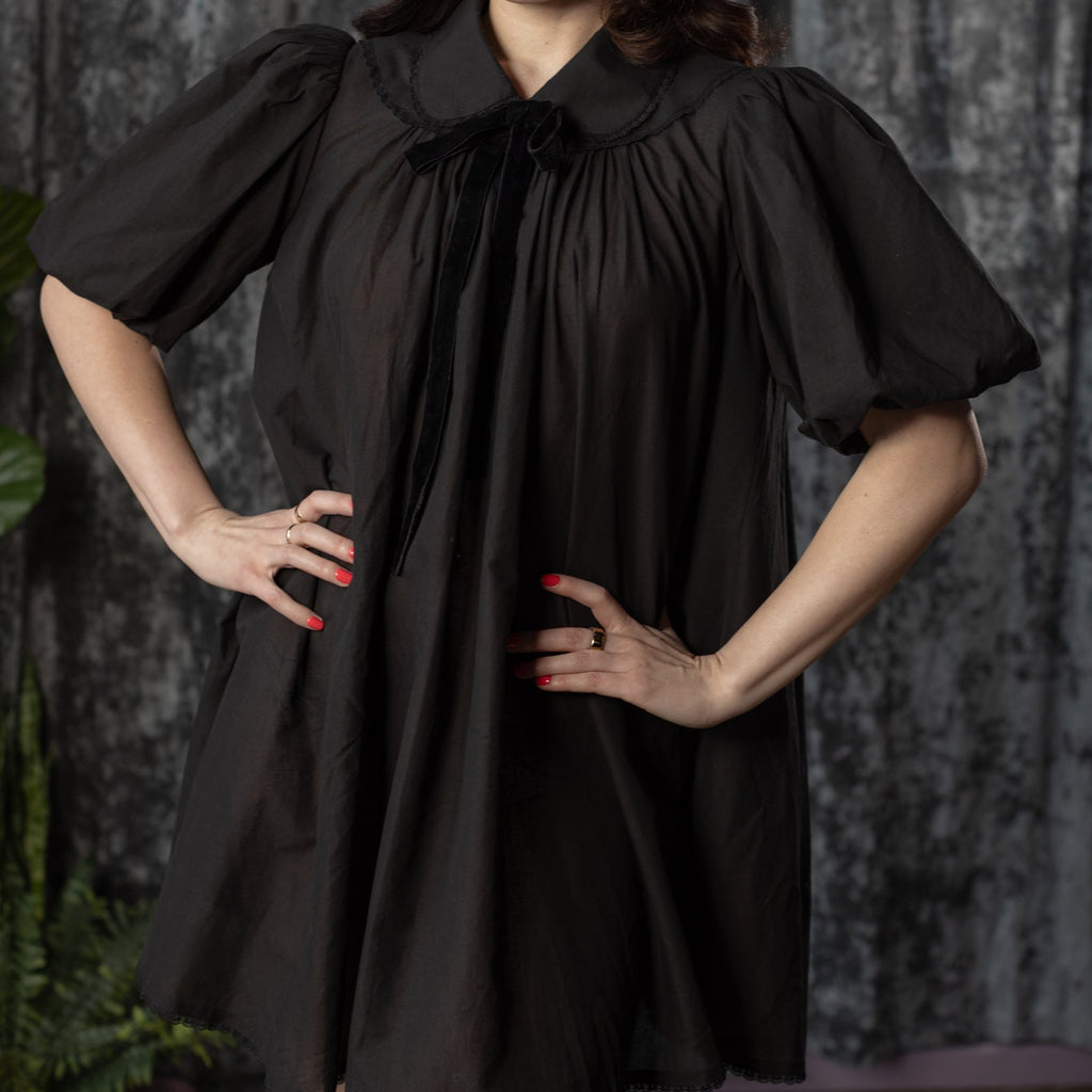 Woman wearing a black dress with a collar against a dark background