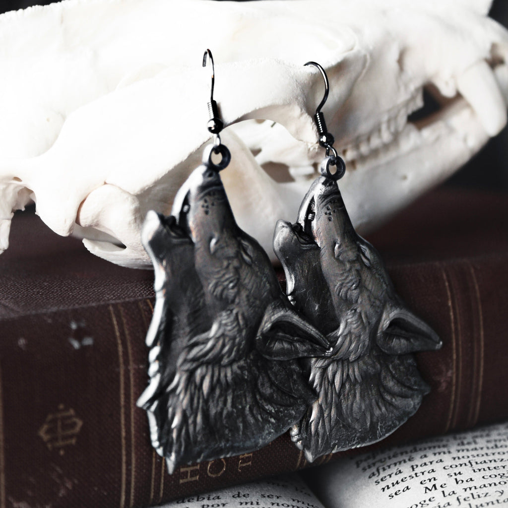 Wolf-shaped earrings on an open book with a skull in the background