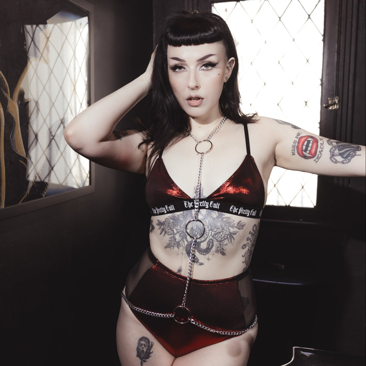 Woman in a red and black outfit with tattoos standing in a dimly lit room.