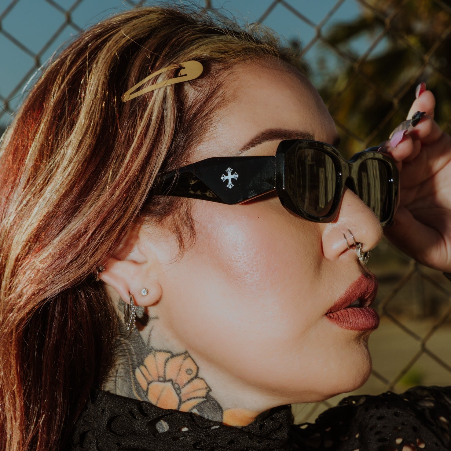 Person wearing sunglasses with a chain-link fence and blurred background