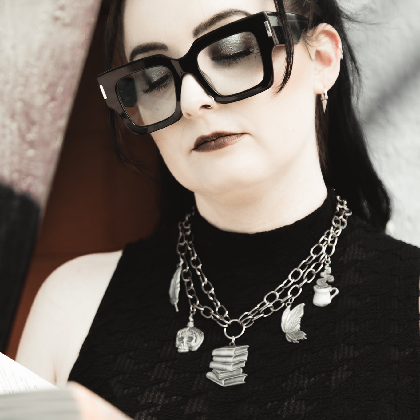 Person wearing a necklace with multiple pendants, holding a book.