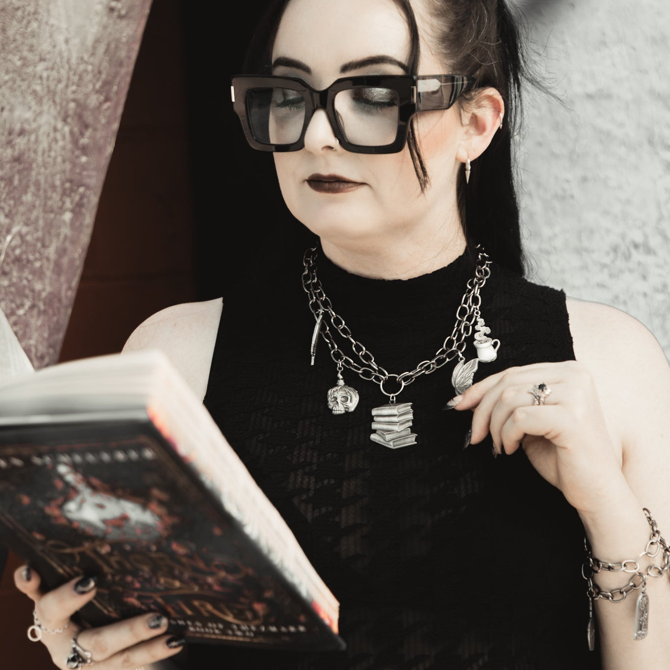Person wearing glasses and a black outfit, holding a book against a neutral background