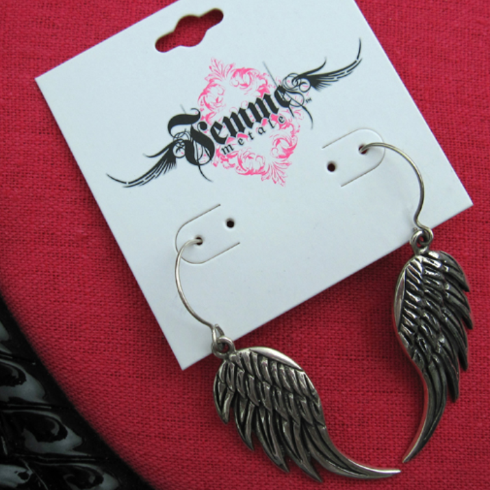 Silver wing-shaped earrings on a branded card against a red background