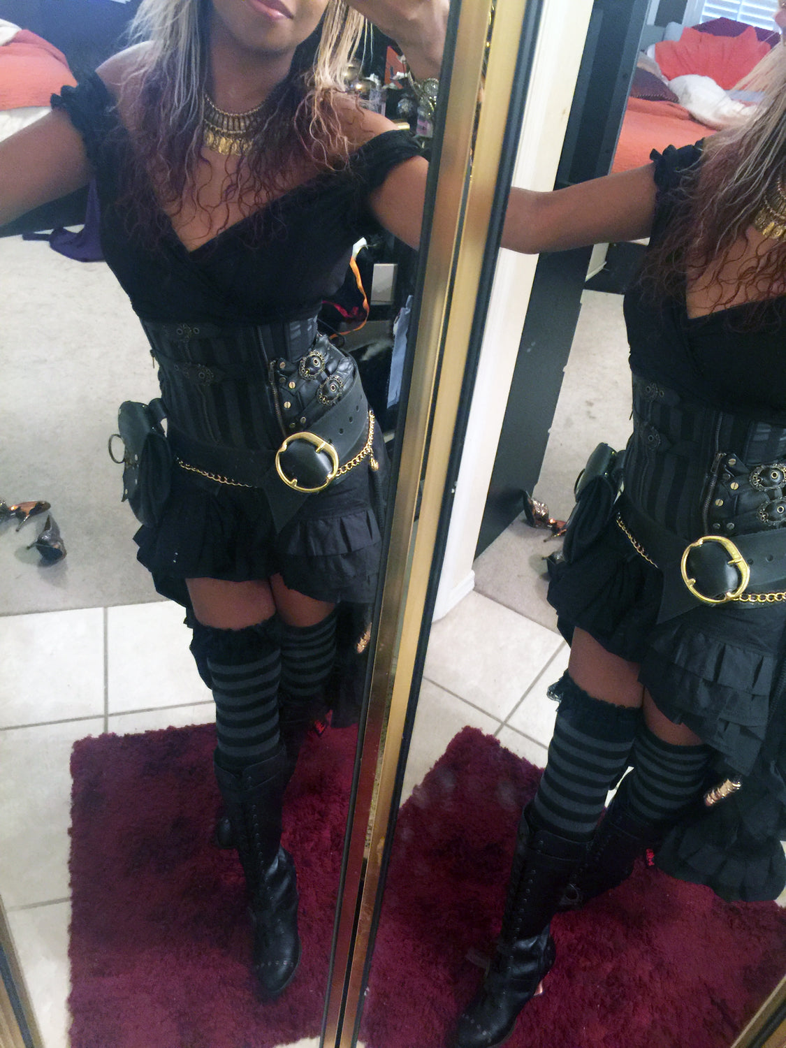 Person wearing a black outfit with gold accents in front of a mirror.