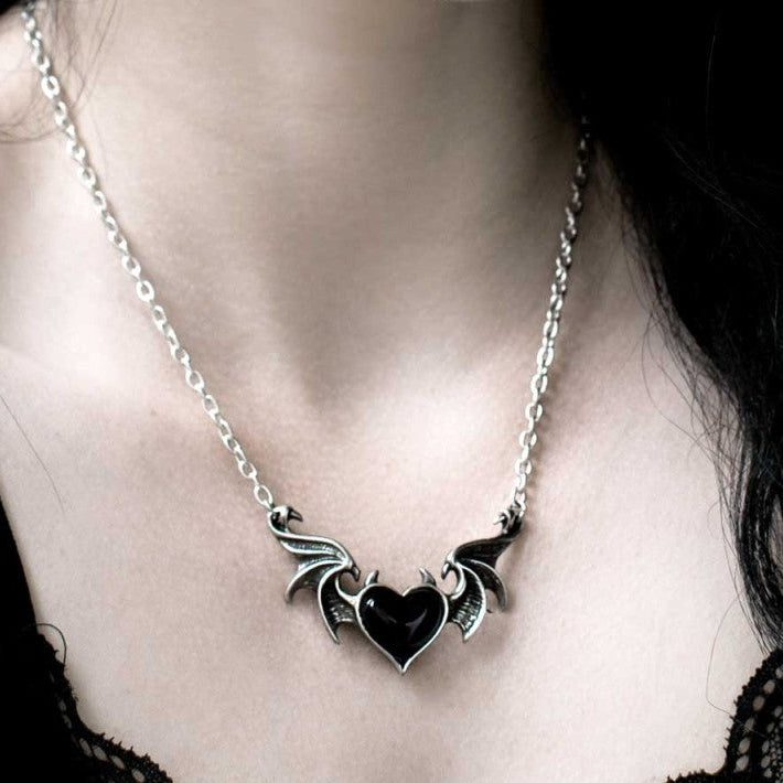 Necklace with a heart and bat design on a person's neck against a dark background