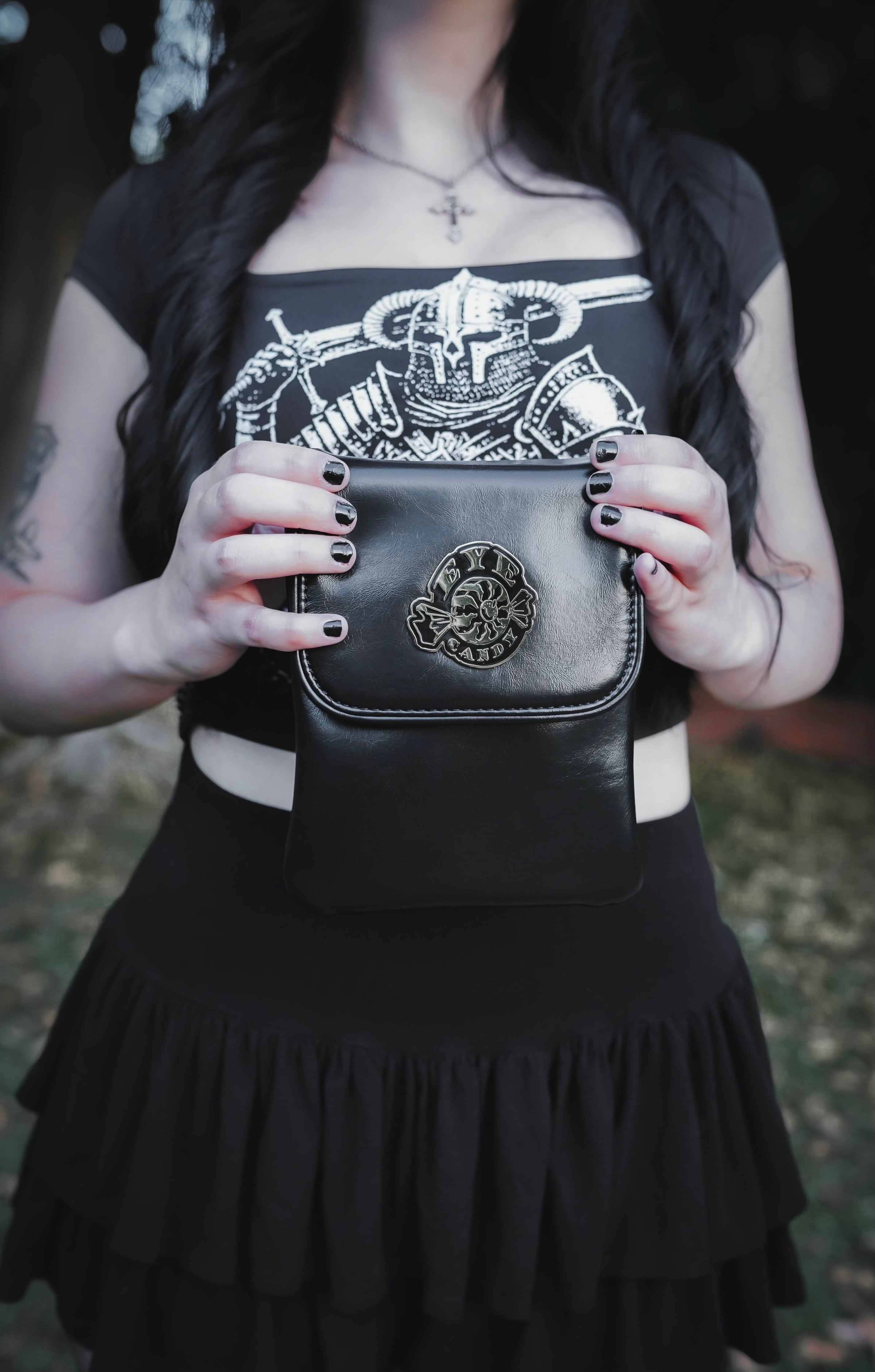 Person holding a black leather bag with intricate design, wearing a black top with white graphic.