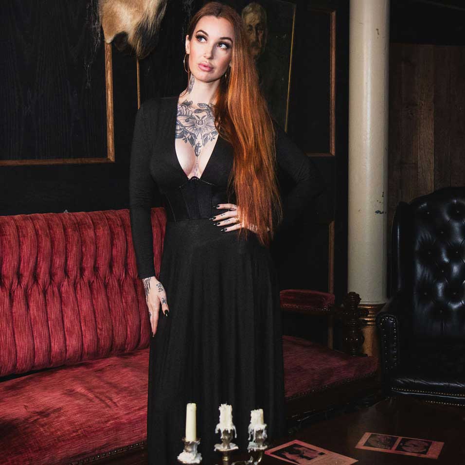 Woman in a black dress standing in an ornate room with red couch and black chair.