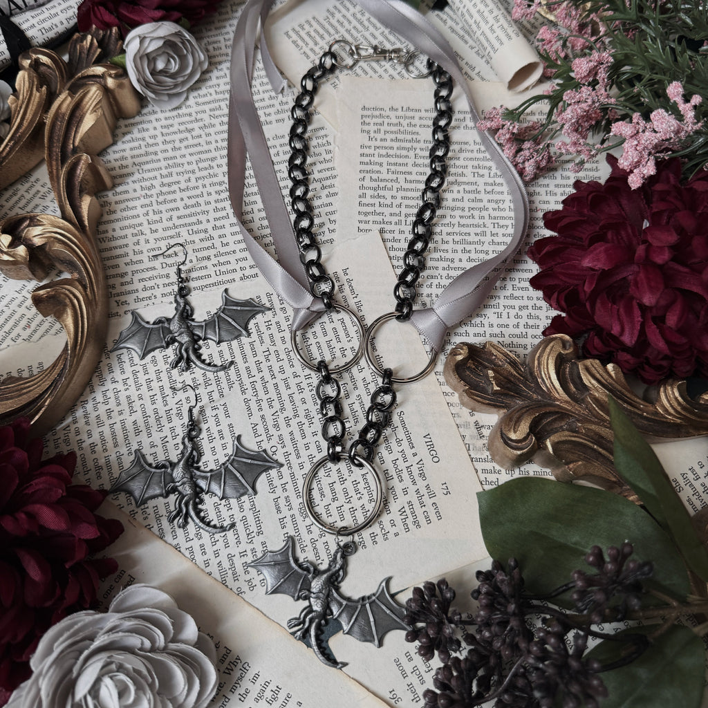 Necklace with bat-shaped pendants on a decorative surface with flowers and an ornate frame.