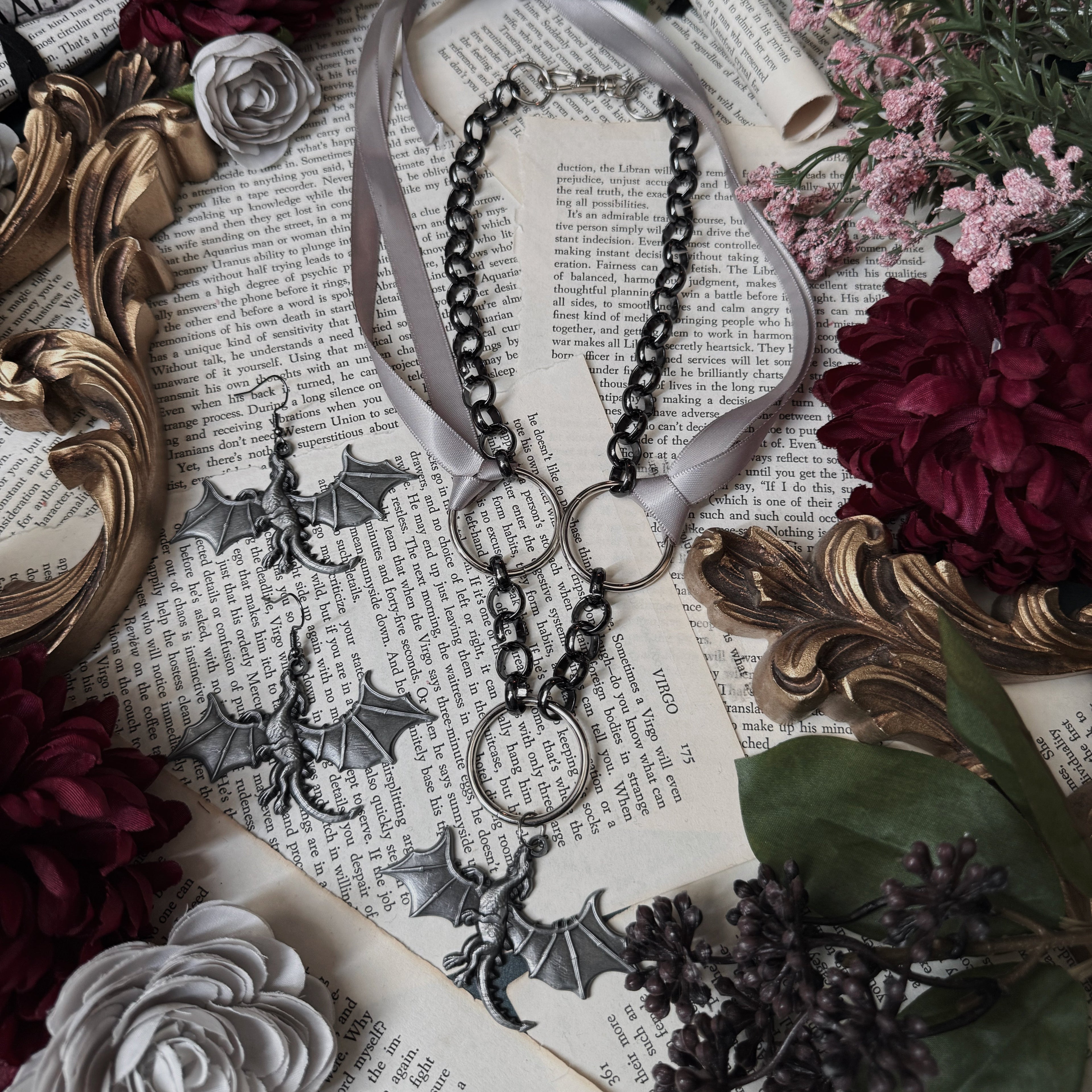 Necklace with bat-shaped pendants on a decorative surface with flowers and an ornate frame.