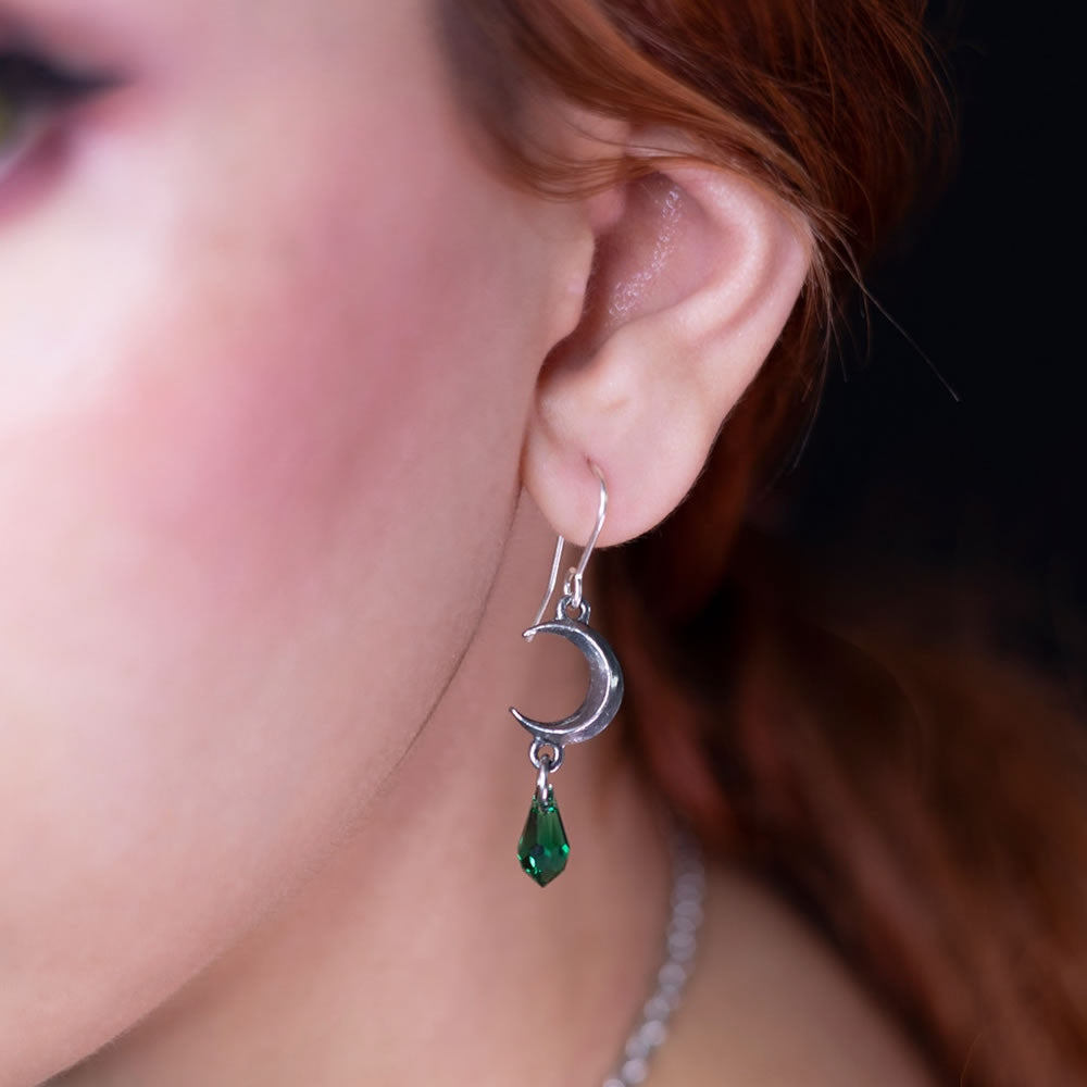Close-up of a person wearing an earring with a green gemstone and moon design.