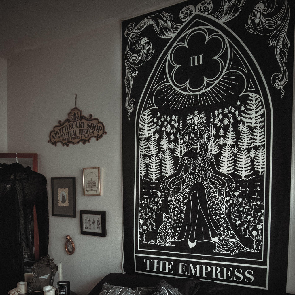 Tapestry titled 'The Empress' hanging on a wall above a couch with decorative pillows.