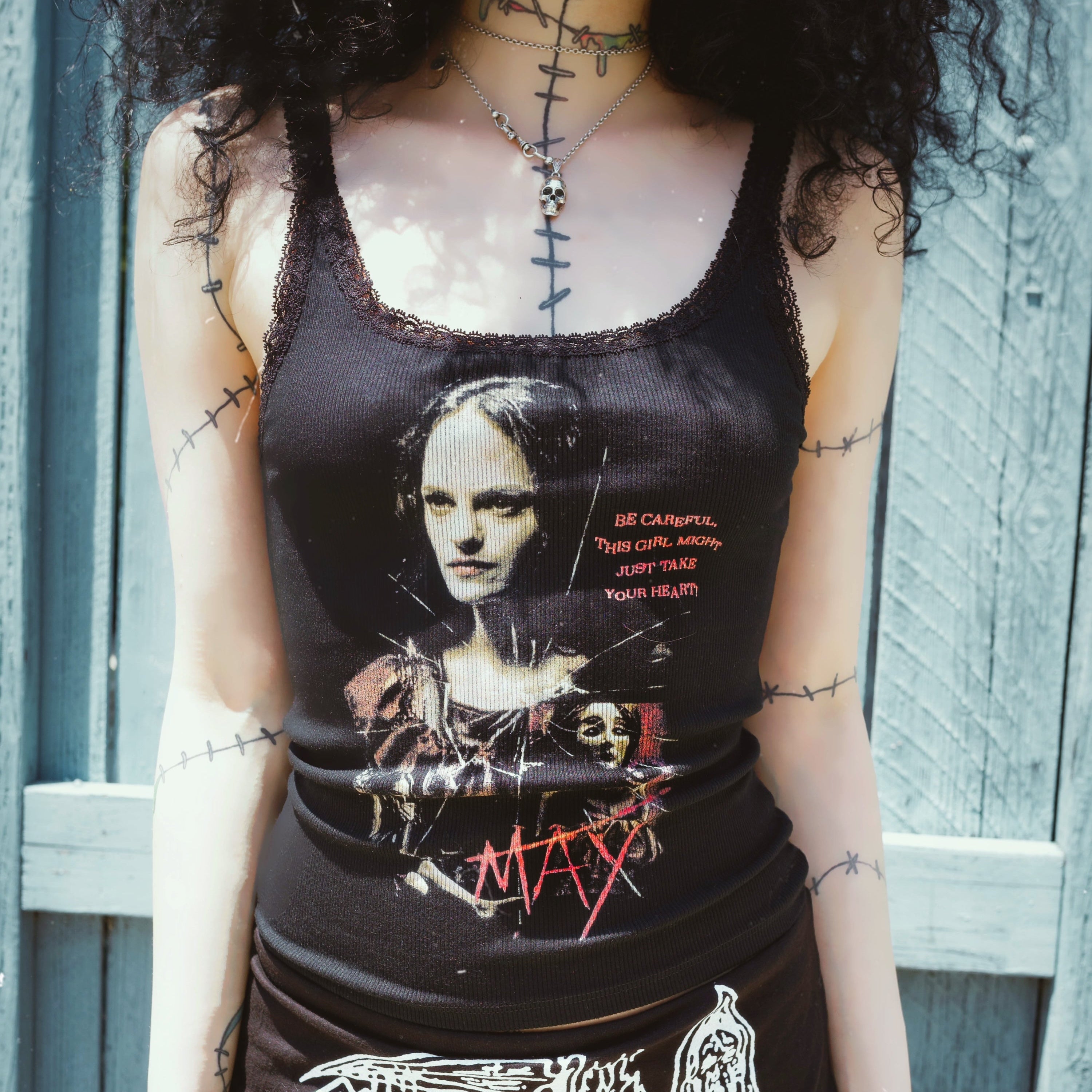 Person wearing a black tank top with graphic design against a wooden fence background