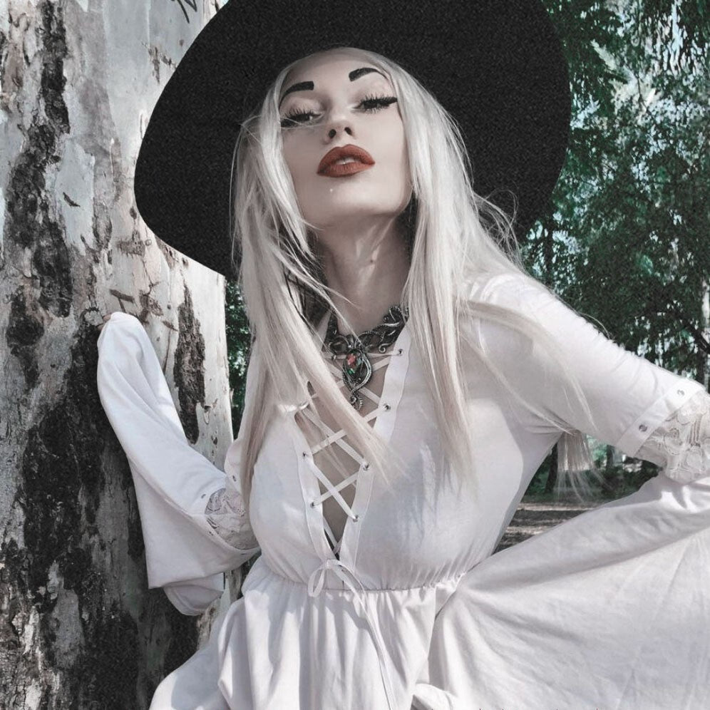 Person with white hair and black hat leaning against a tree in a natural setting