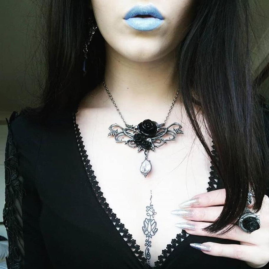 Person wearing a black lace top with a gothic-style necklace featuring a rose pendant.