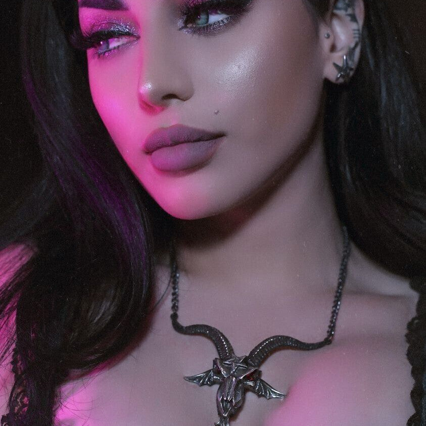 Woman wearing a black lace top and a necklace with a bird design, illuminated by pink light.