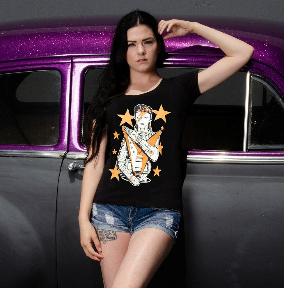 Woman wearing a black t-shirt with a graphic design, standing next to a purple and black vehicle.