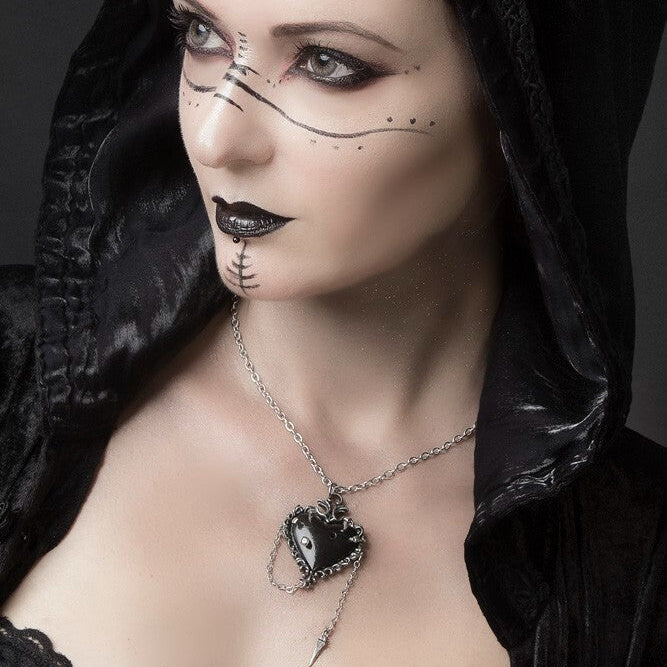 Woman wearing a black hooded garment with dark makeup and a necklace, against a dark background.
