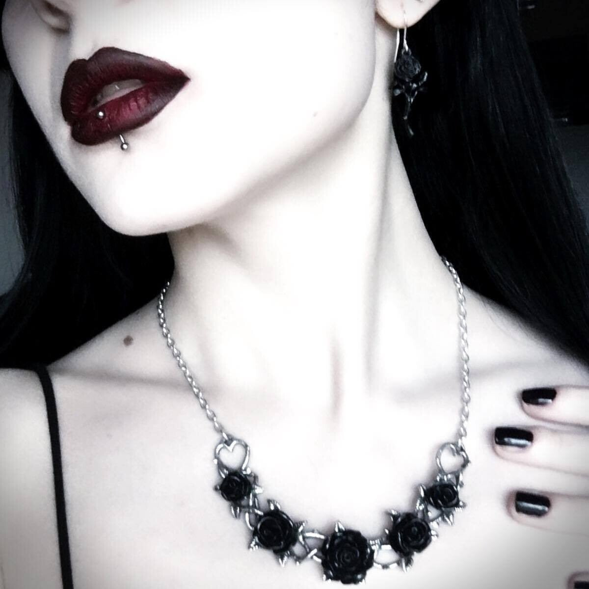 Close-up of a woman wearing a black floral necklace with dark lipstick and long dark hair.