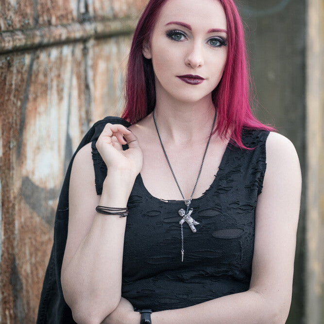 Woman with pink hair wearing a black top and plaid skirt against a textured wall.