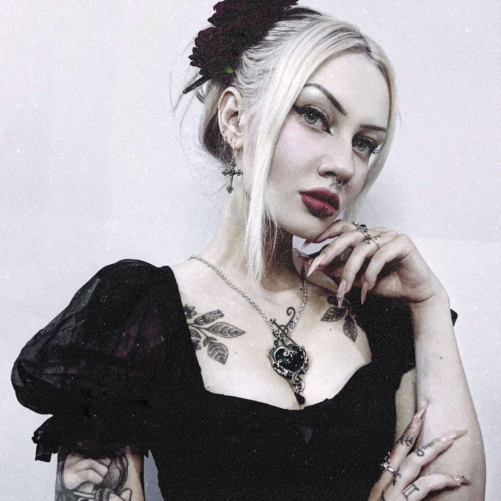Woman with tattoos wearing a black top against a white background