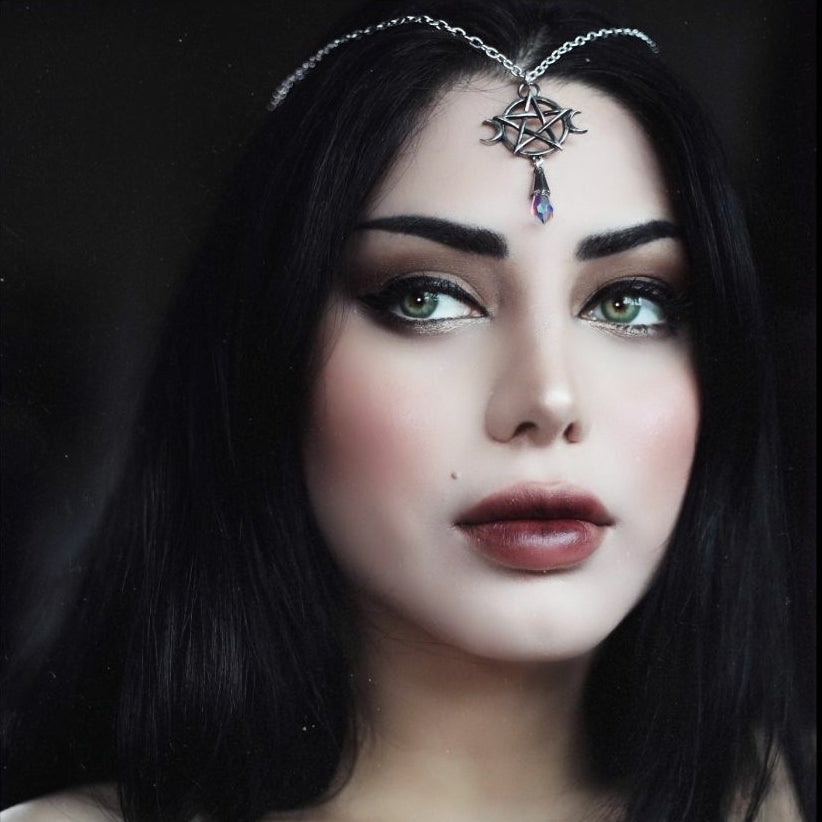 Woman with dark hair and makeup wearing a headpiece with a pentagram design.