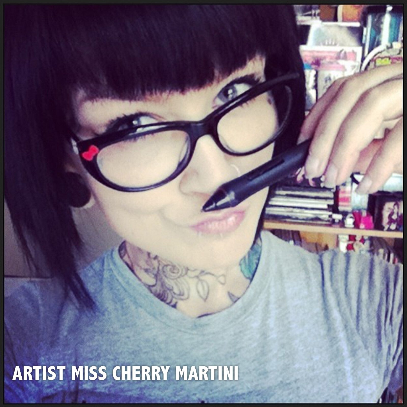 Person with tattoos holding a pen, with 'Artist Miss Cherry Martini' text overlay