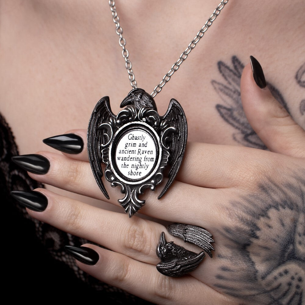 Necklace with an angelic pendant held by a hand with black nail polish and tattoos.