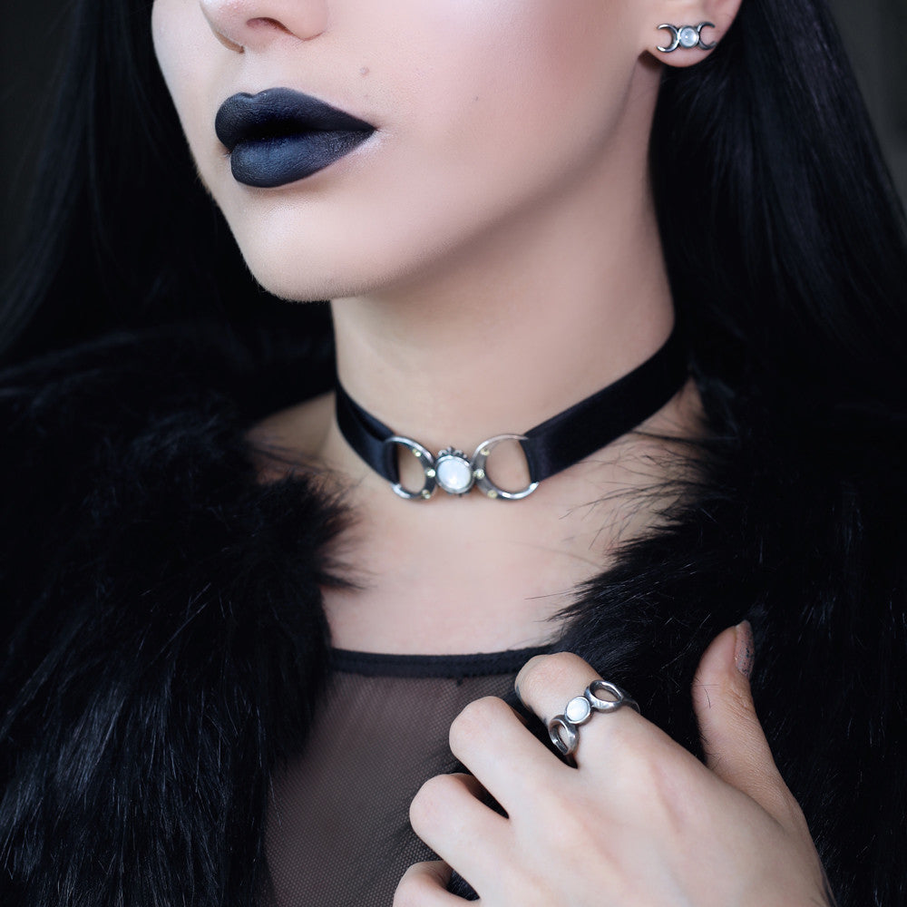 Close-up of a person wearing a black choker with a silver clasp, dark lipstick, and black fur.