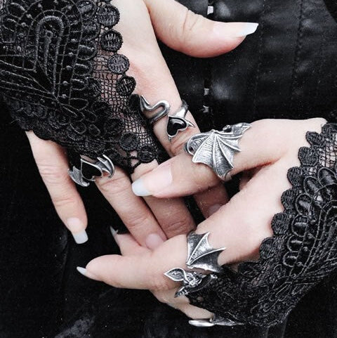 Close-up of hands wearing black lace gloves and silver rings with a dark background