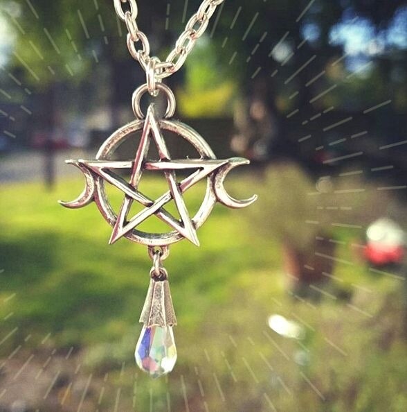 Silver pentagram pendant with a teardrop-shaped crystal on a blurred outdoor background