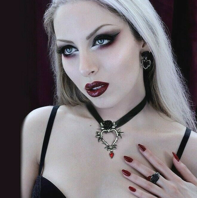 Woman with gothic makeup and attire, wearing a heart-shaped necklace.