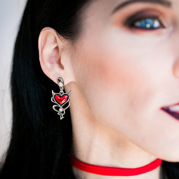 Close-up of a woman wearing a red choker and heart-shaped earrings with 'Alchemy' branding.