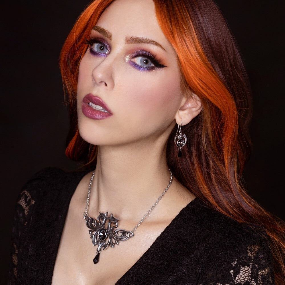 Woman with red hair and purple makeup wearing a black lace top and silver necklace against a dark background