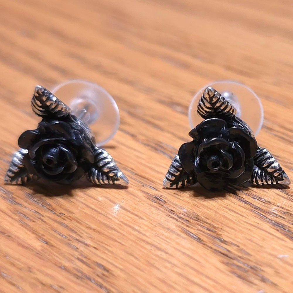 Black rose earrings with silver accents on a wooden surface
