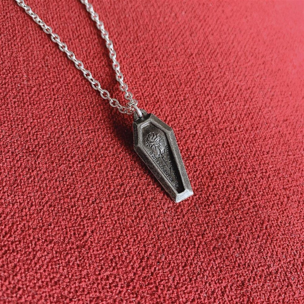 Coffin-shaped pendant on a chain against a red fabric background