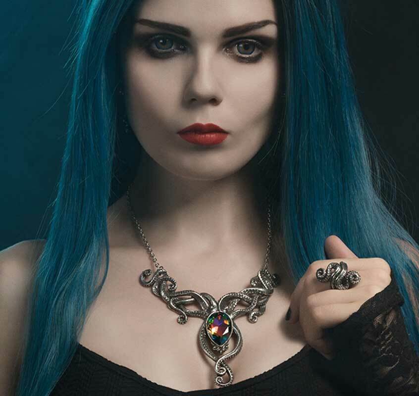 Woman with blue hair wearing a detailed necklace and ring against a dark background
