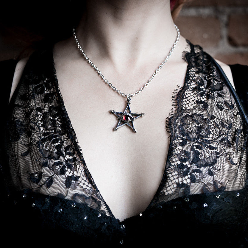 Person wearing a black lace top with a star pendant necklace against a brick wall.