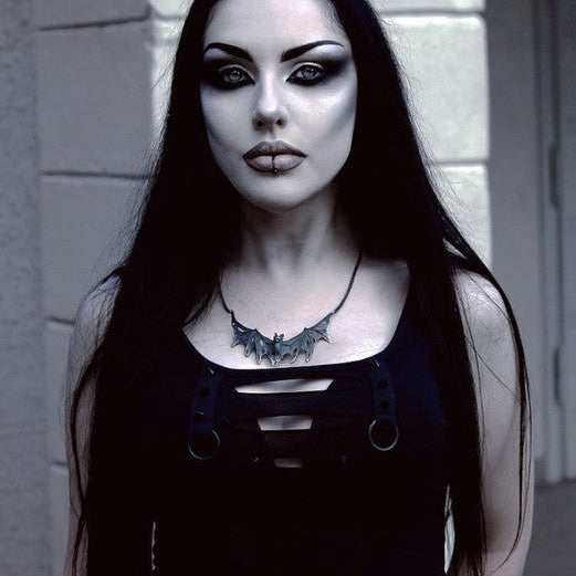 Person with dark makeup and black clothing against a gray wall