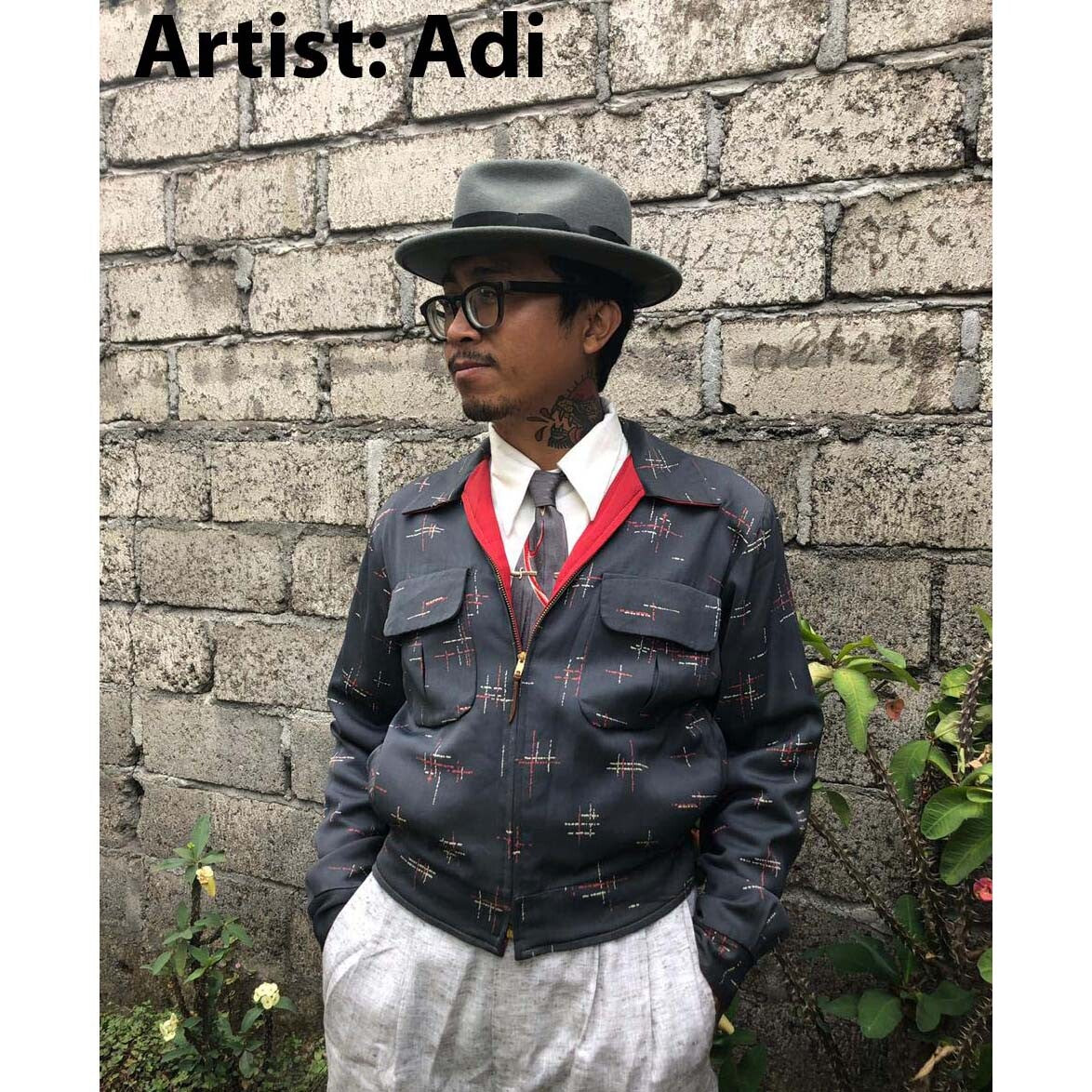 Person wearing a patterned jacket and hat against a brick wall