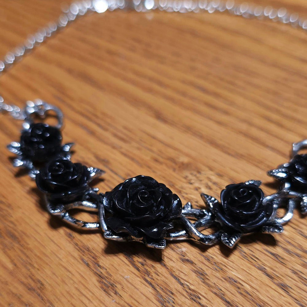 Necklace with black rose pendants on a wooden surface