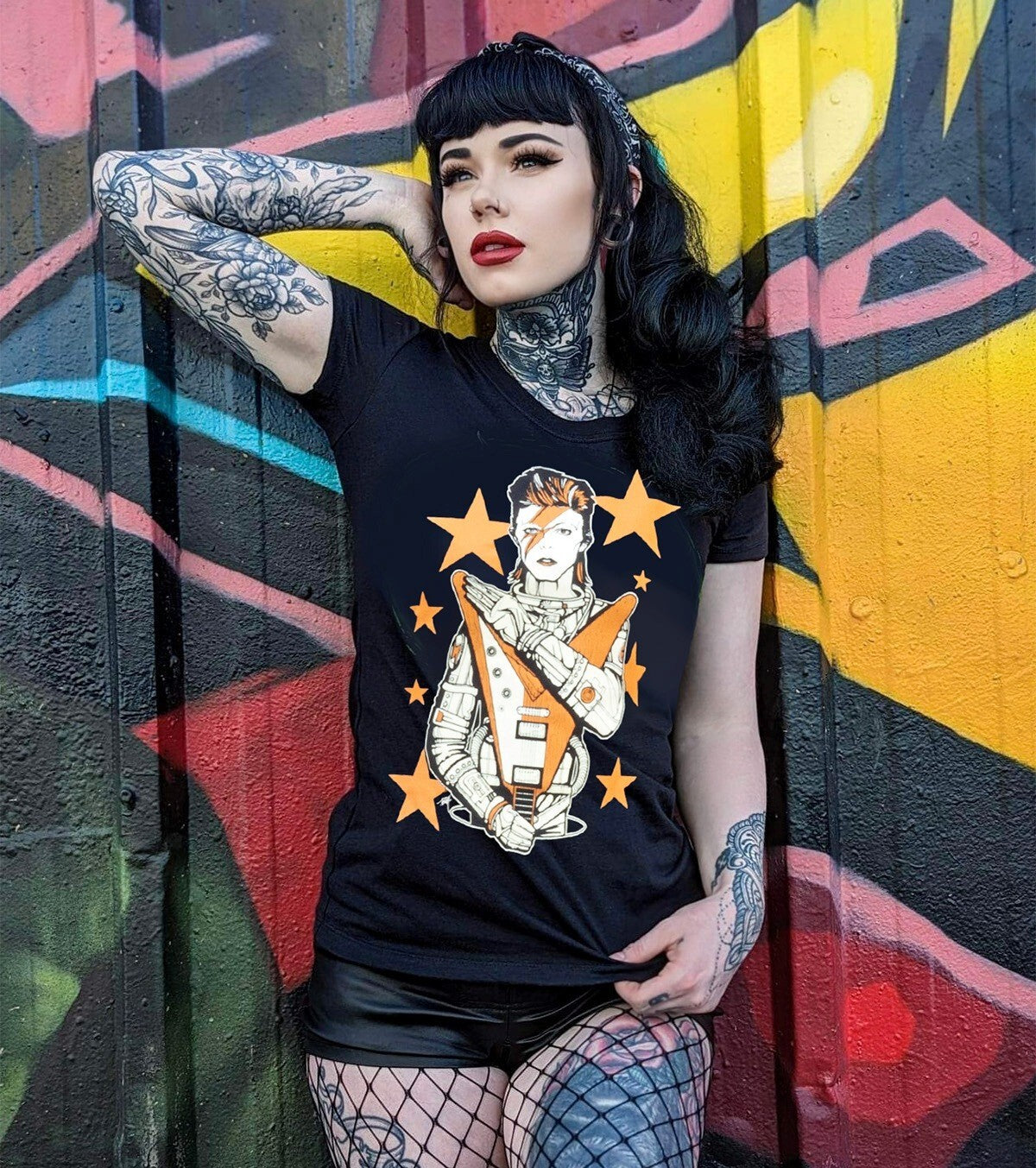 Person wearing a black t-shirt with a graphic design, standing against a colorful graffiti wall.
