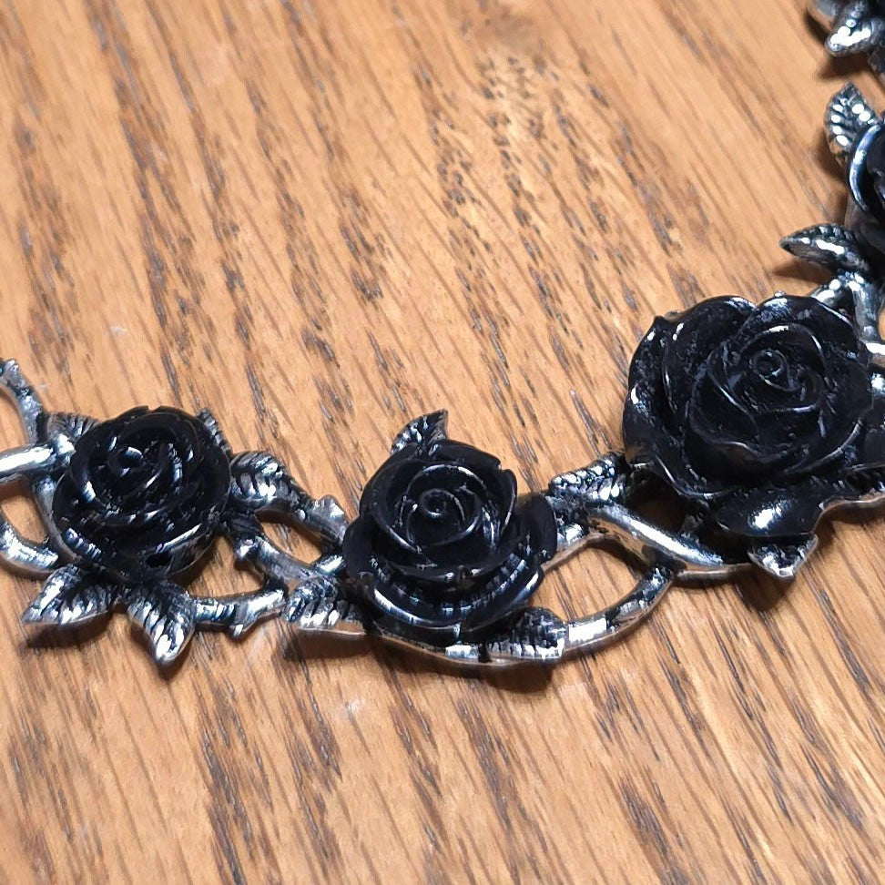 Bracelet with black rose flowers and silver metalwork on a wooden surface