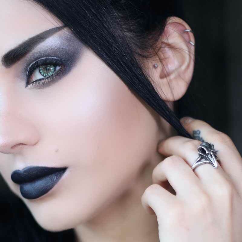 Close-up of a person with dark hair and makeup, wearing a silver ring.