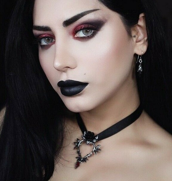 Woman with dark lipstick and smoky eye makeup wearing a black choker with a rose pendant.