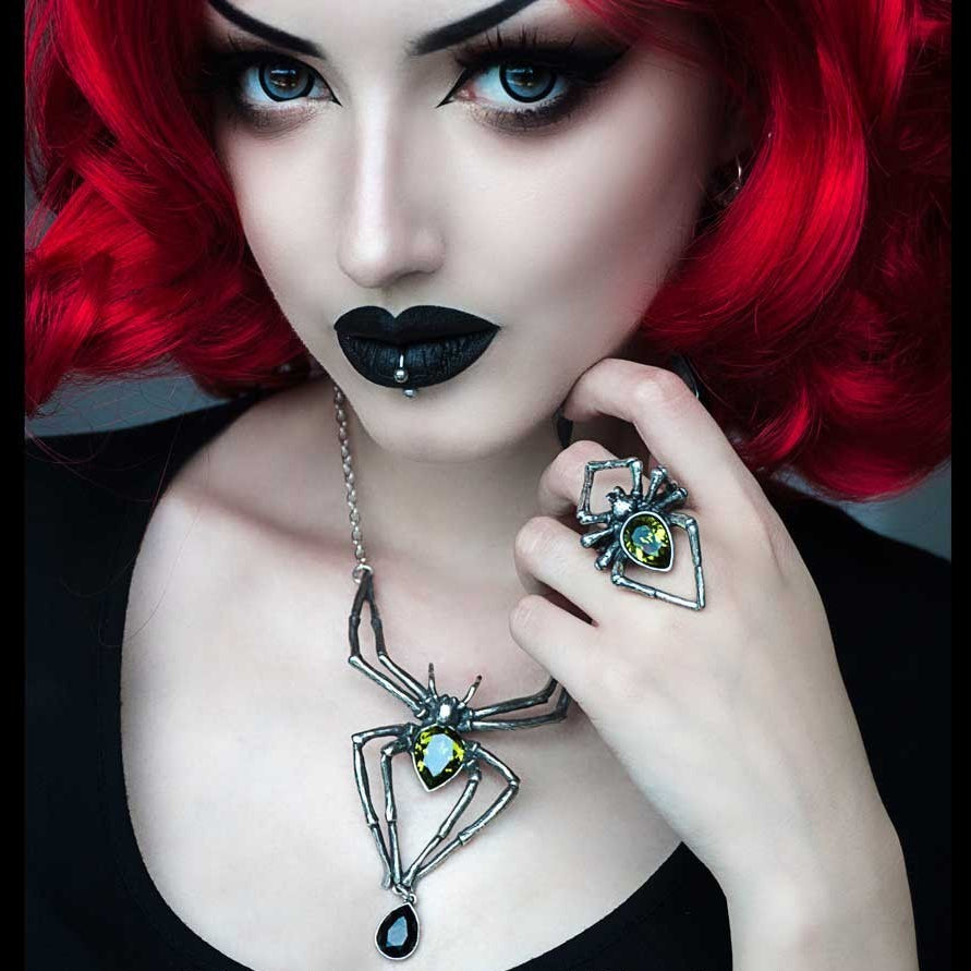 Woman with red hair wearing a necklace and ring with gemstones, brand 'Alchemy Carta' visible