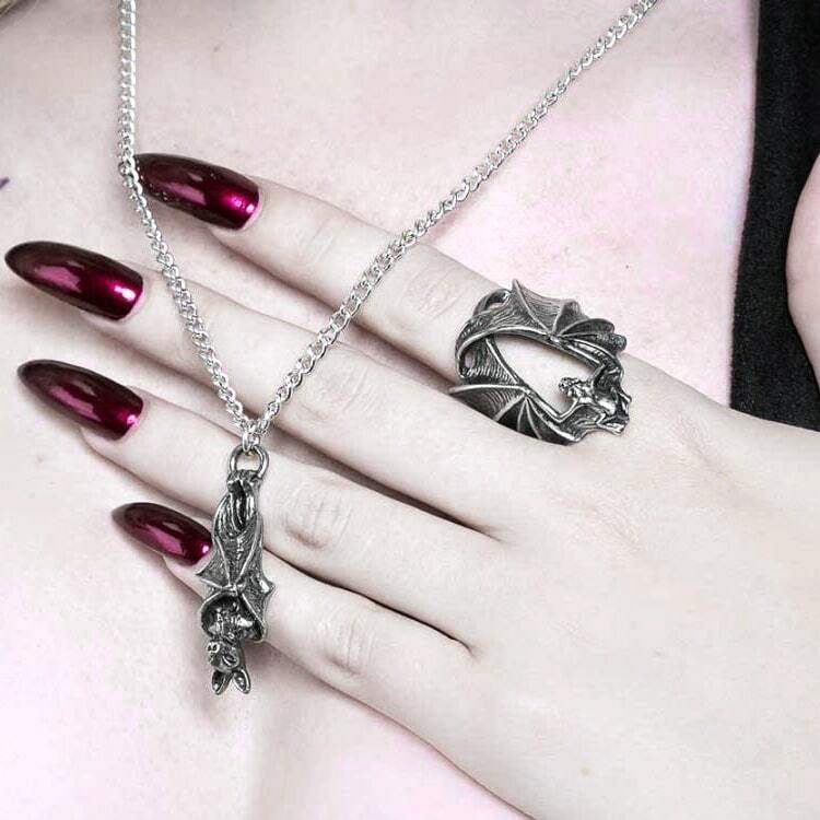Silver necklace and ring on a hand with red nail polish against a light background