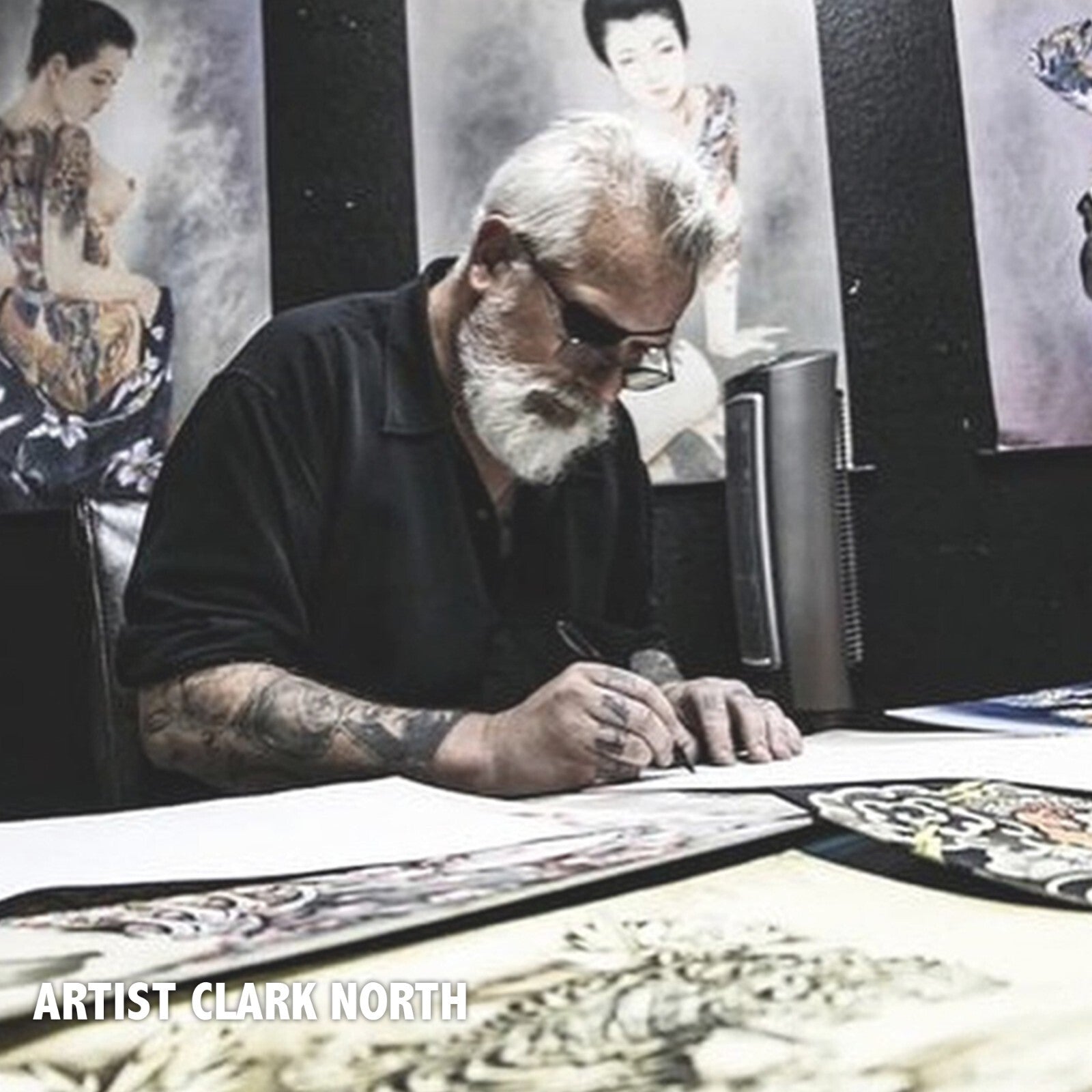 Artist Clark North working on a tattoo design with tattoos and artwork in the background.