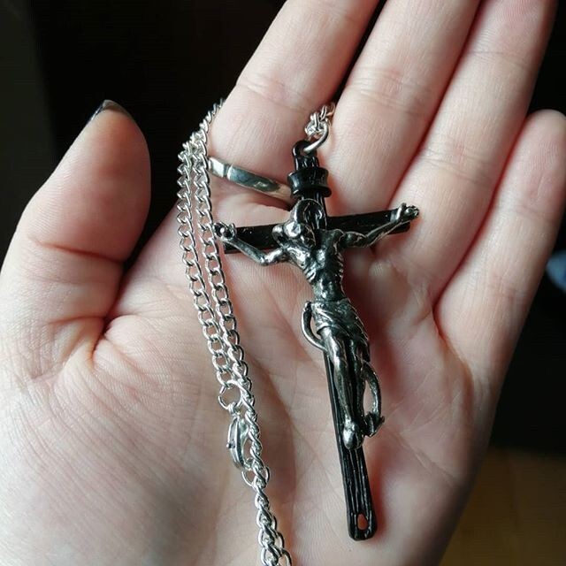 Silver crucifix pendant on a chain held in a hand against a neutral background