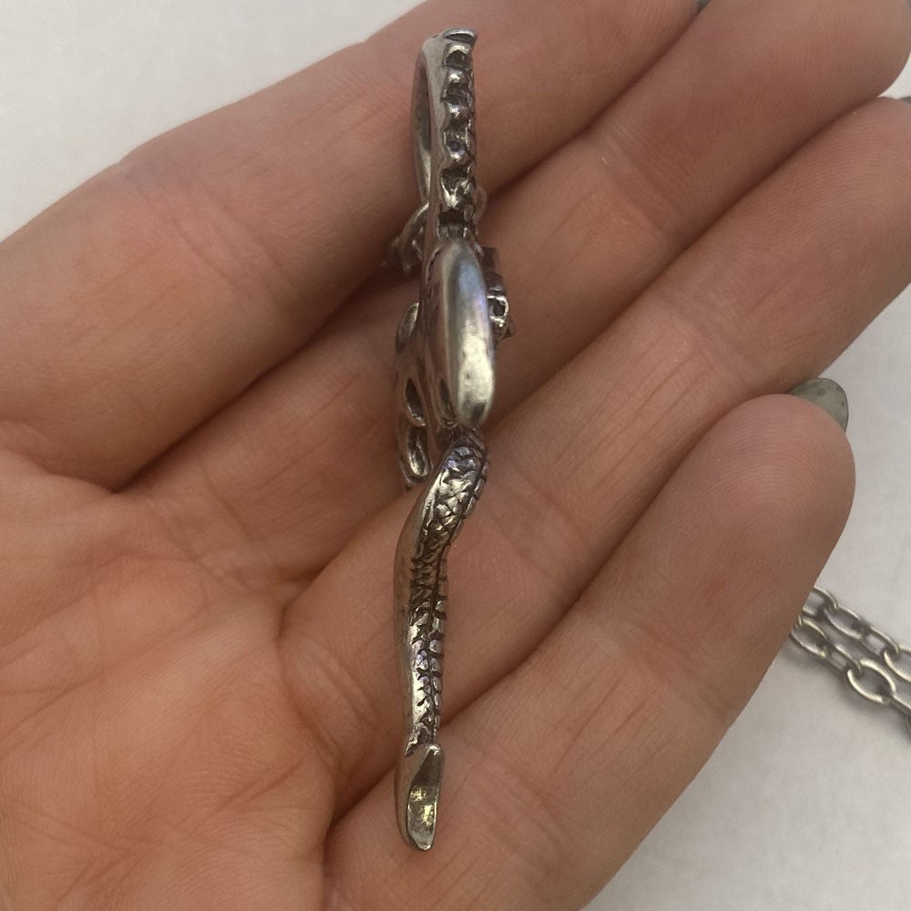 Silver snake pendant held in a hand against a white background